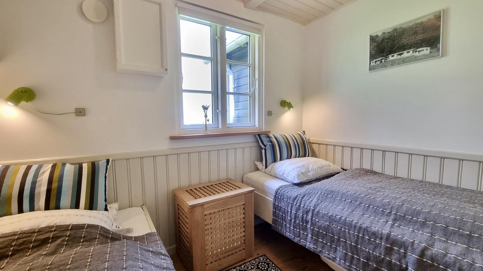 Zwei Einzelbetten mit bunten Kissen und Holzkommoden. Fenster mit Blick nach draußen.