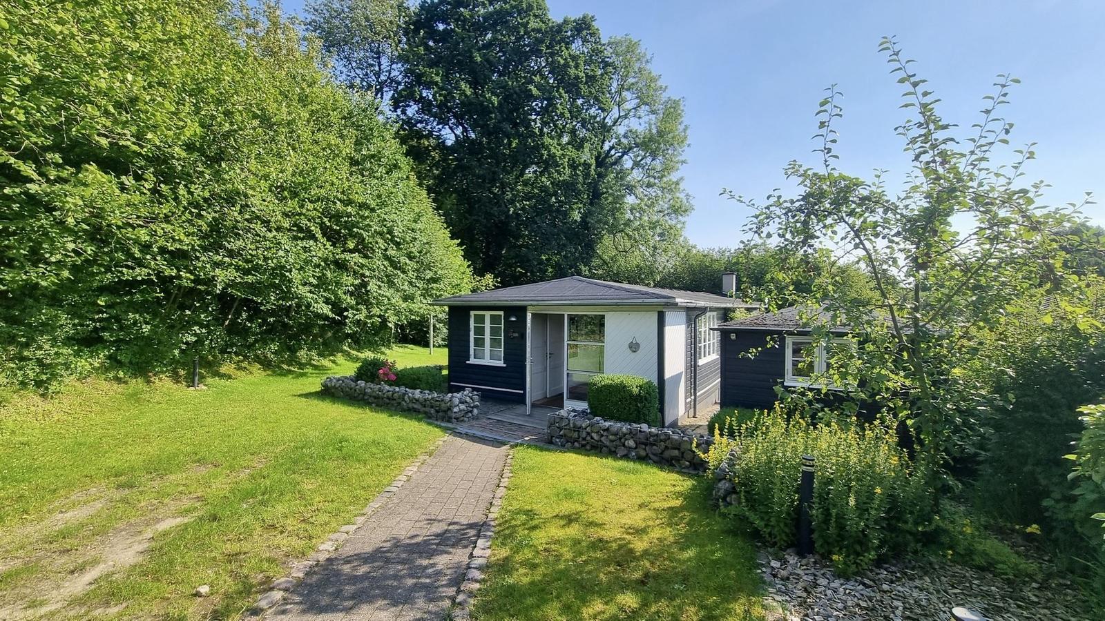 Ein kleines Haus mit dunklem Holz und weißer Fassade, umgeben von Grün und Bäumen.