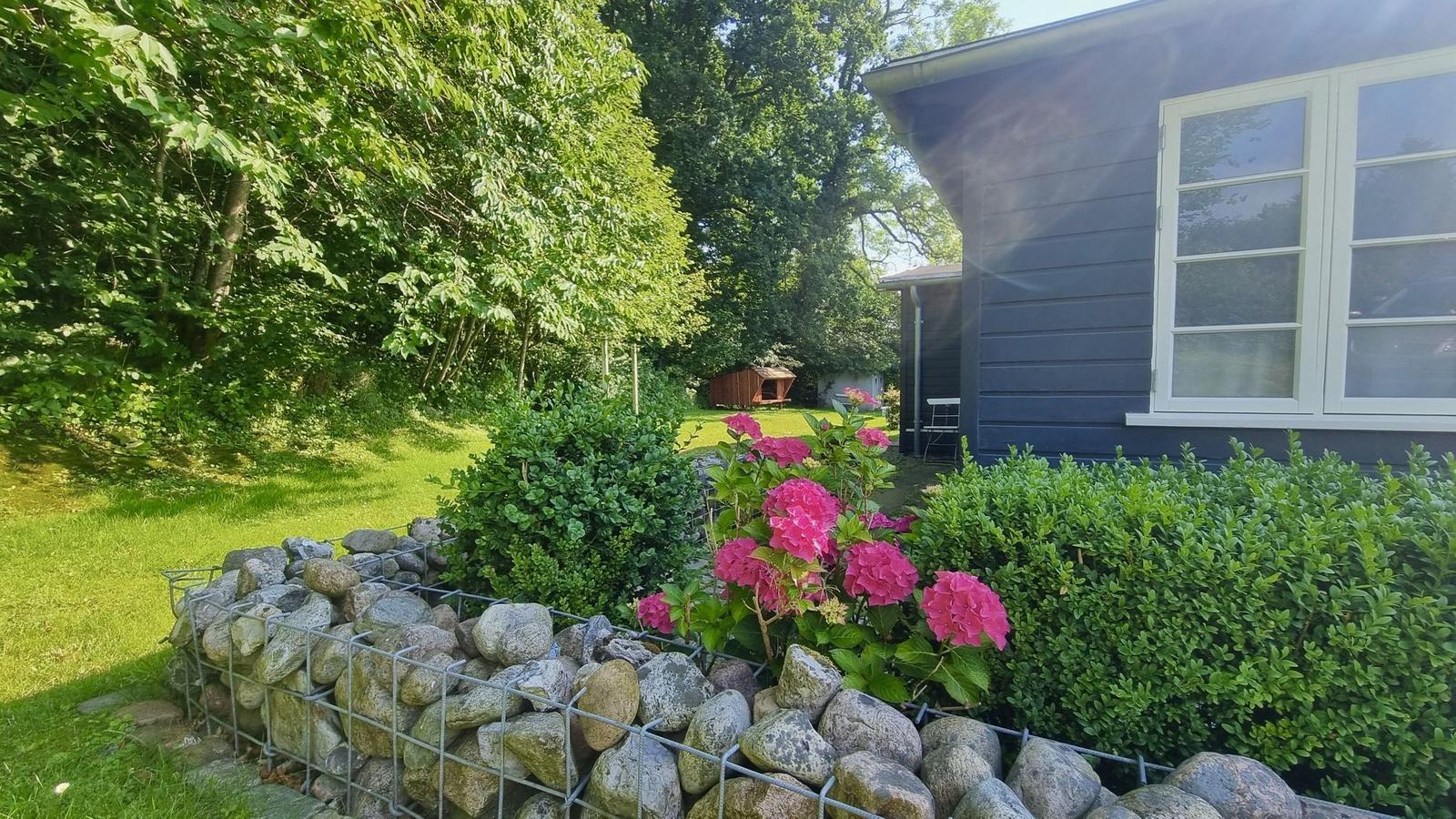 Blauer Holzhaus mit Garten, Blumen und Steinmauer.