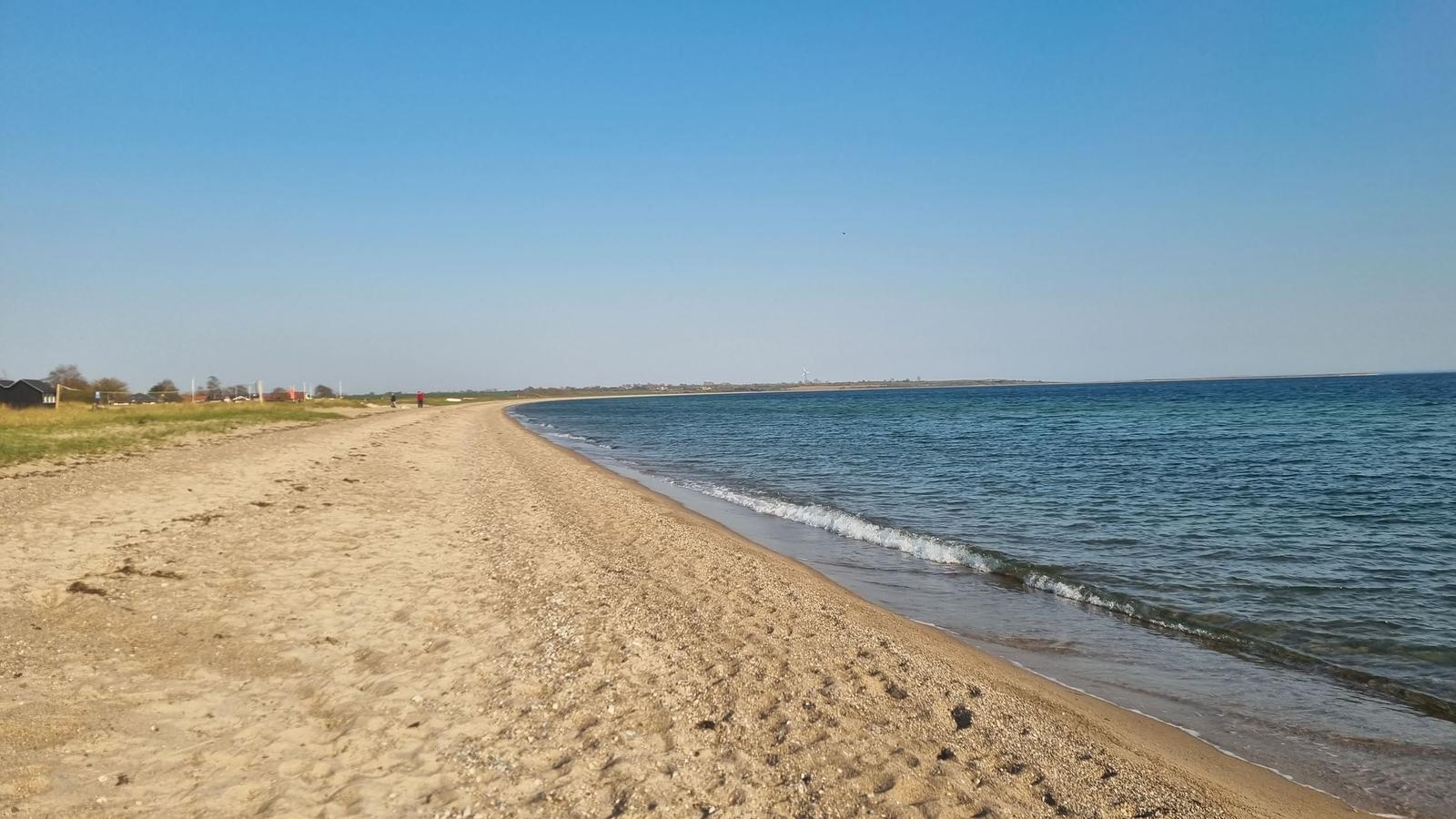 Strand mit Sand und ruhigem Meer unter blauem Himmel