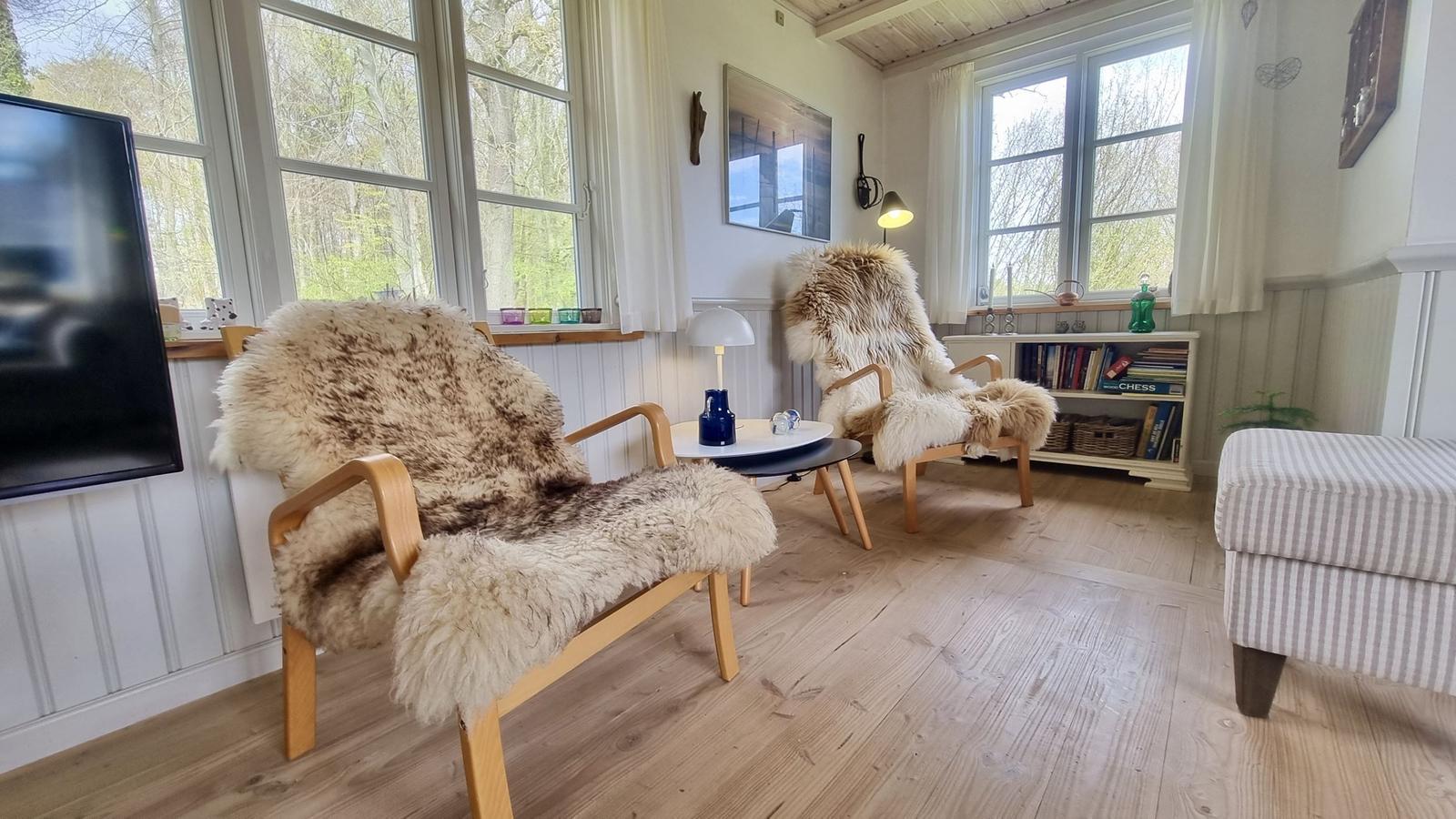 Zwei Sessel mit Felldecken, Couchtisch und Bücherregal im Wohnzimmer.