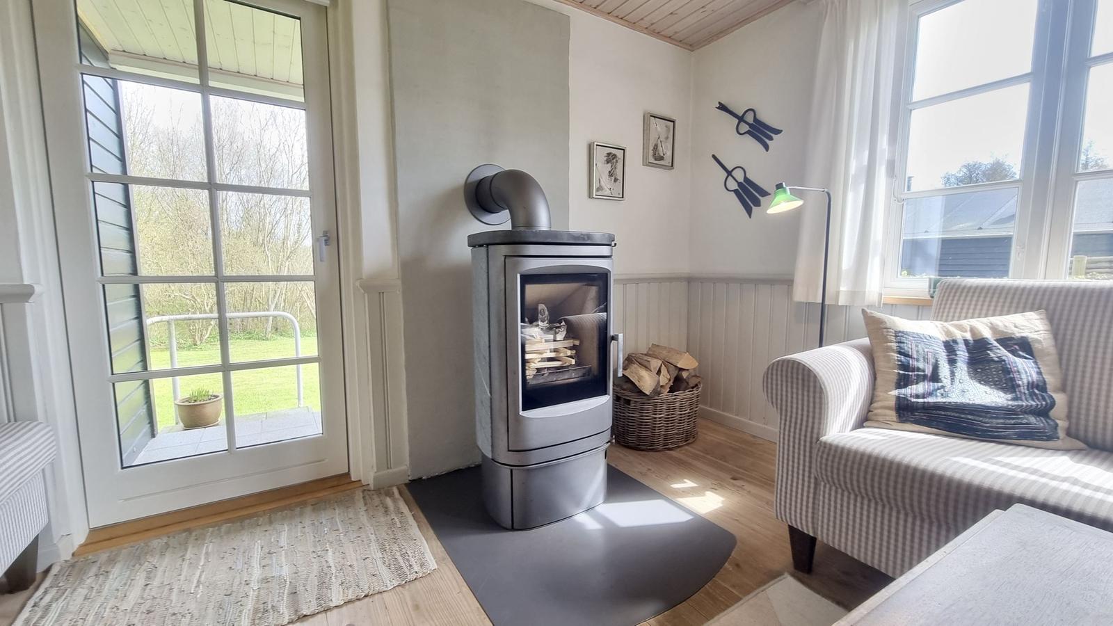 Wohnzimmer mit Kaminofen, Sofa und Blick auf die Terrasse.