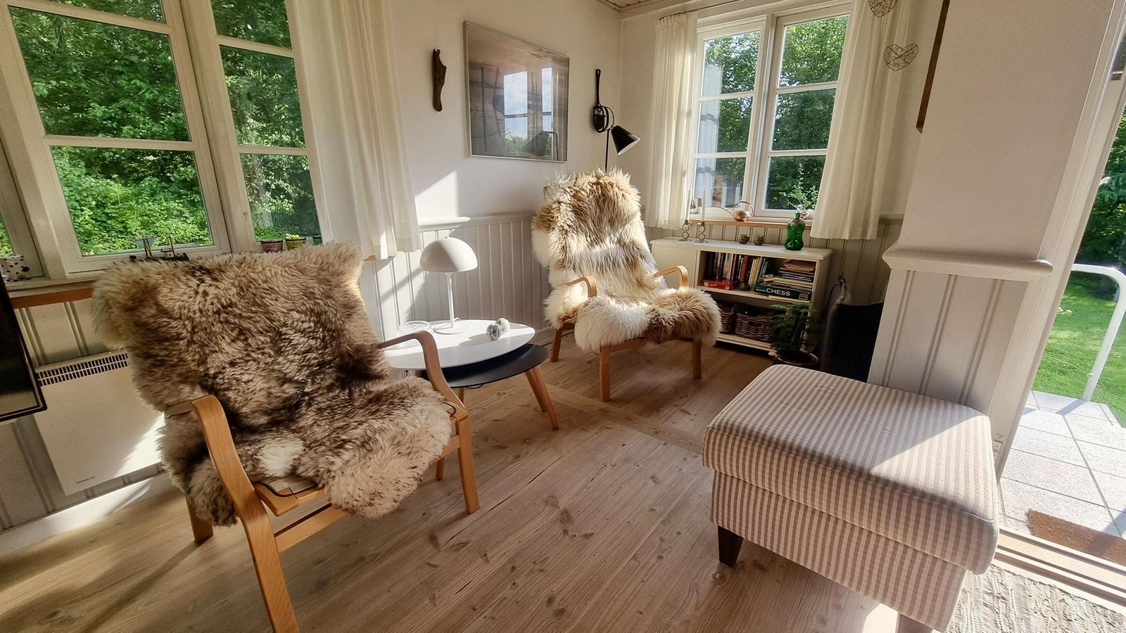 Zwei Stühle mit Felldecken, Tisch und Sessel im Raum mit Fenstern.