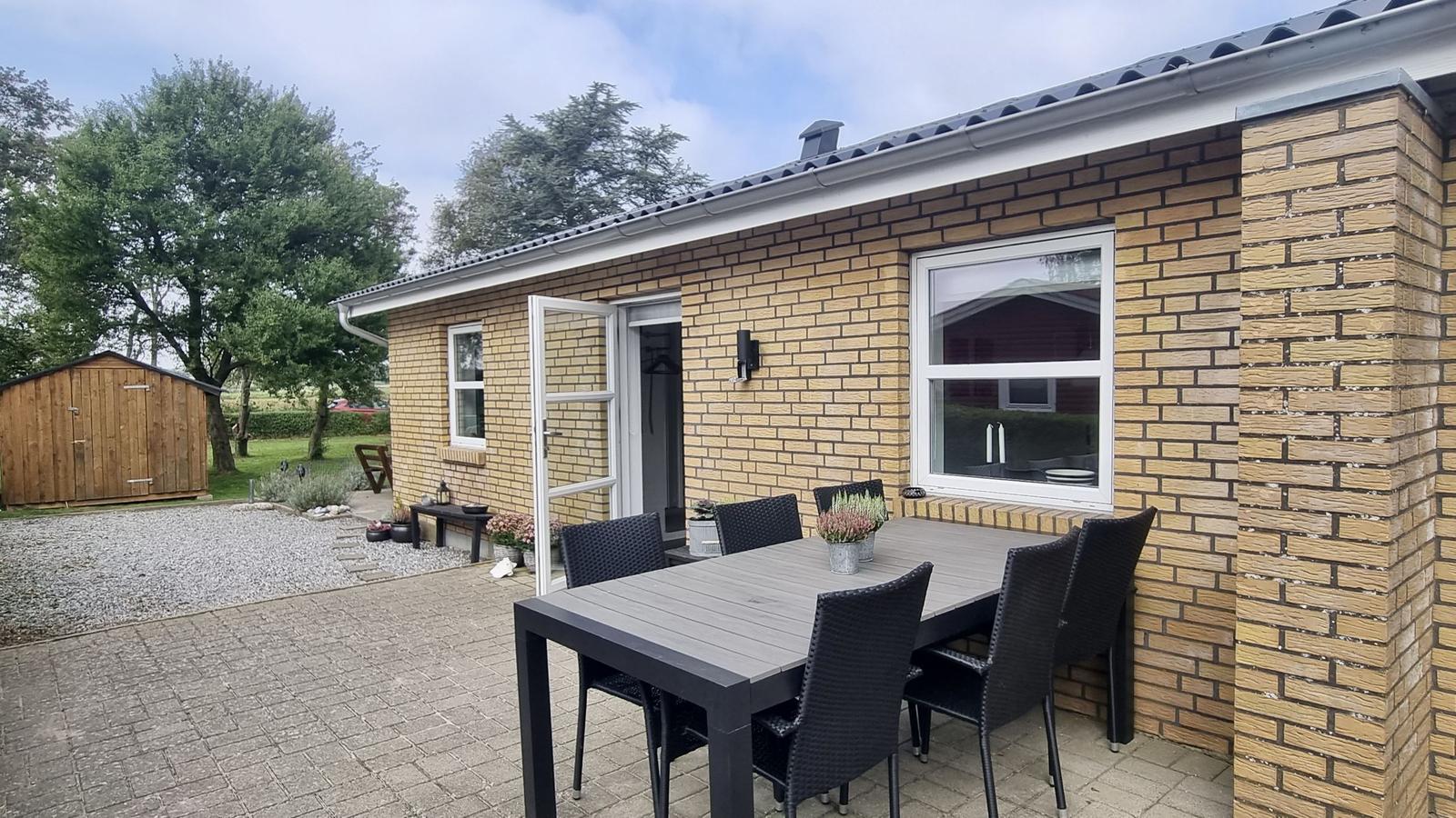 Terrasse mit Tisch und Stühlen vor einer Backsteinfassade mit offener Tür.