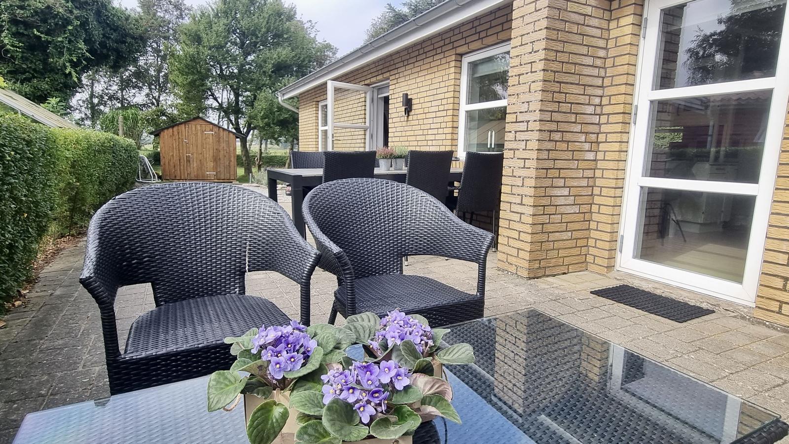 Terrasse mit Gartenmöbeln und Blumen vor einem Haus.