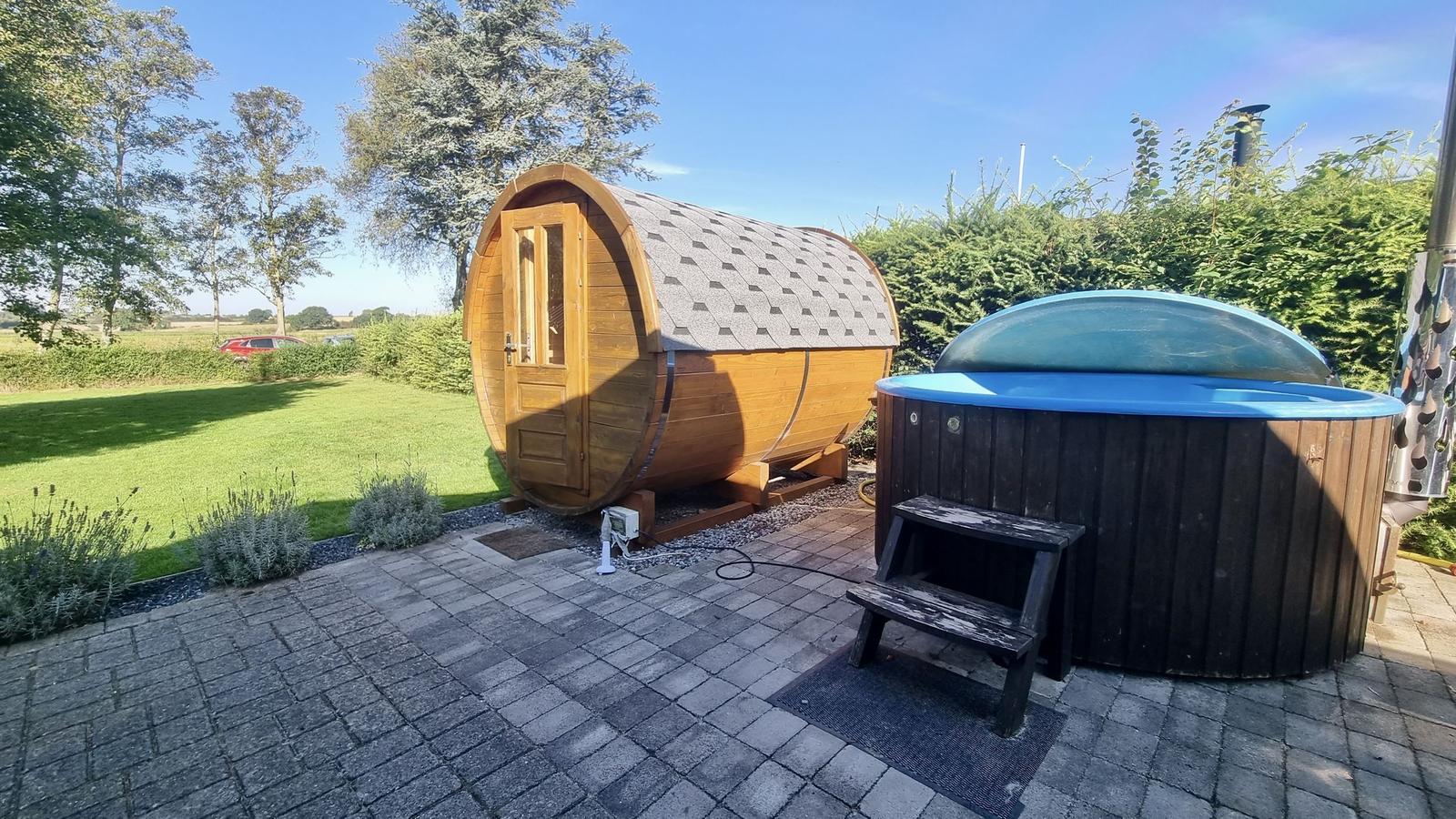 Holz-Sauna und Whirlpool auf Terrasse mit Garten und Bäumen.