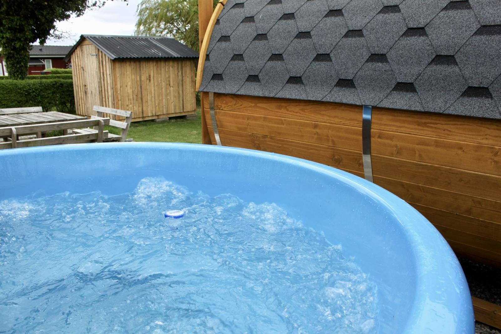Blauer Whirlpool mit sprudelndem Wasser im Garten neben einem Holzhaus.