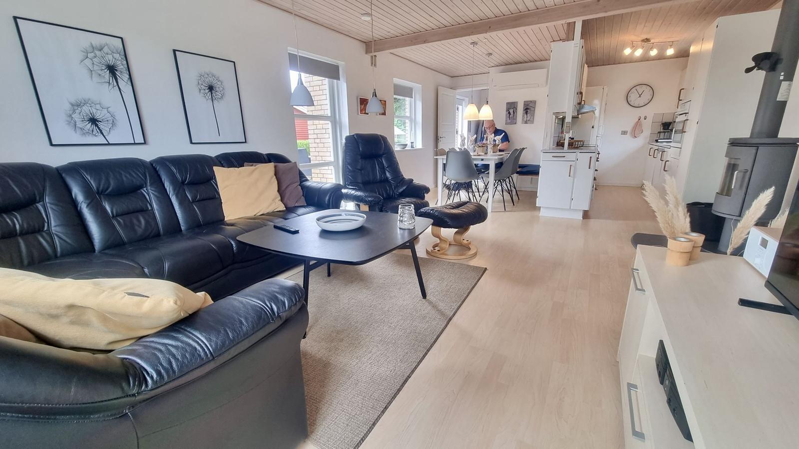 Wohnzimmer mit Sofa, Couchtisch und Essbereich. Küche und Kamin im Hintergrund.