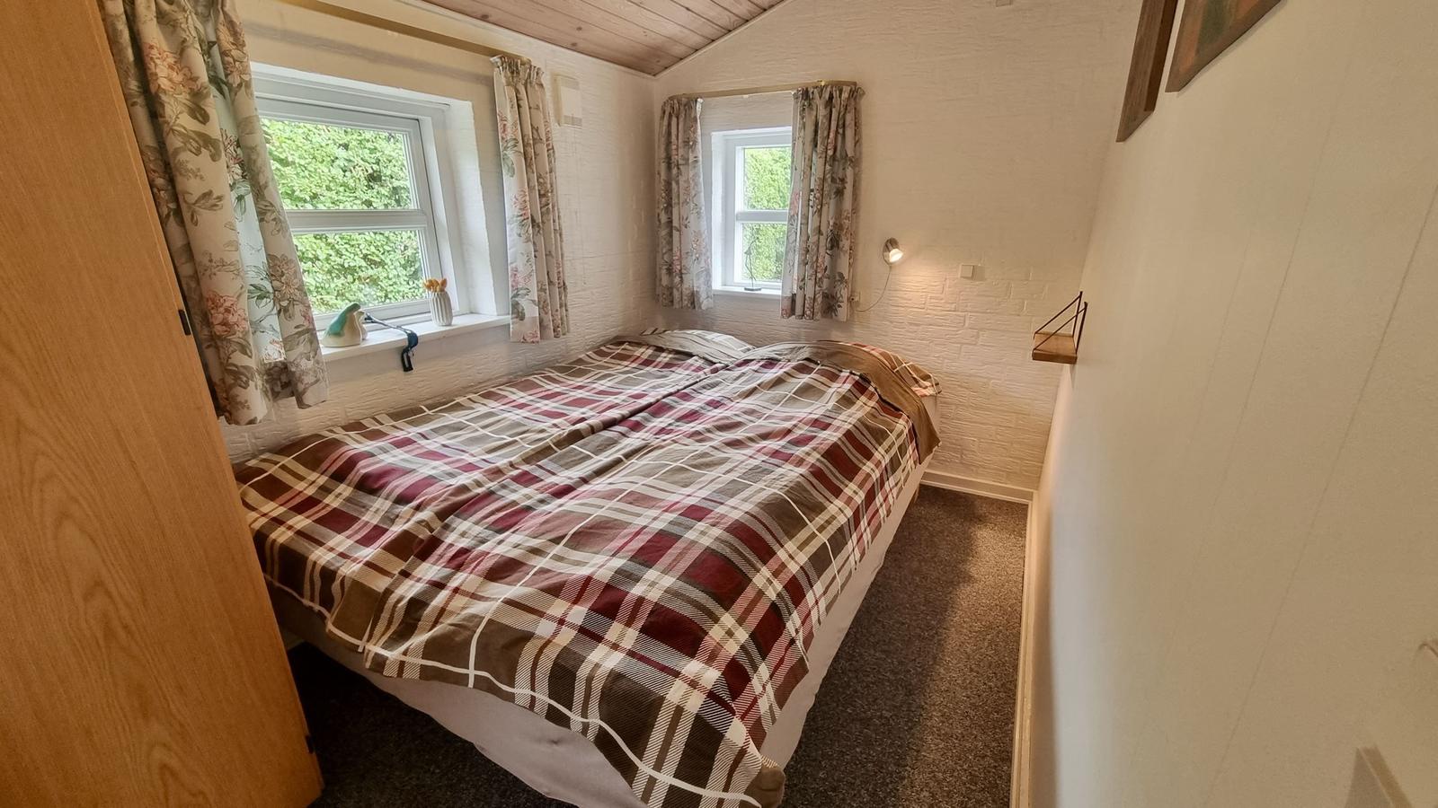 Schlafzimmer mit Doppelbett, zwei Fenstern und Holzdecke.