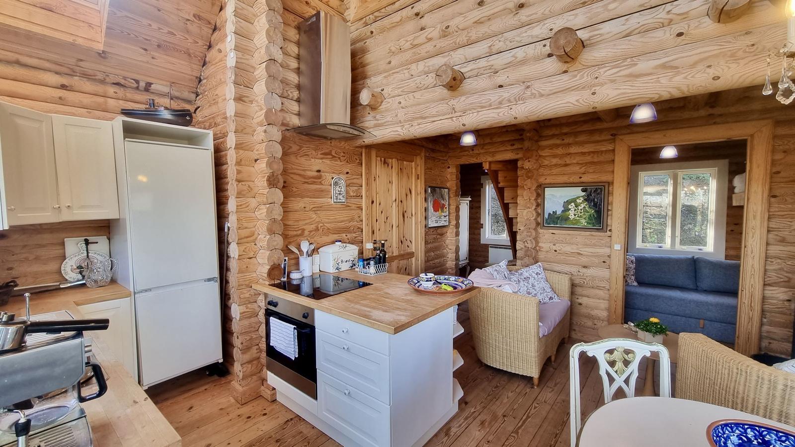 Küche mit Essbereich und Wohnzimmer in Holzhaus. Kühlschrank, Herd und Sofa sichtbar.