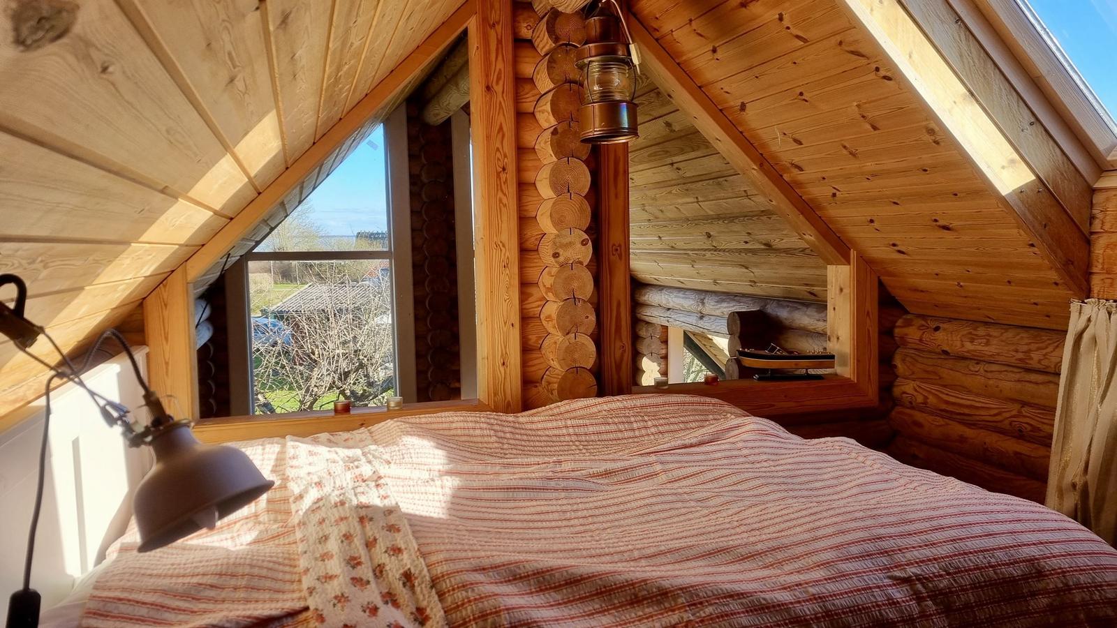 Schlafzimmer mit Holzwand, Fenster und Bett unter Dach