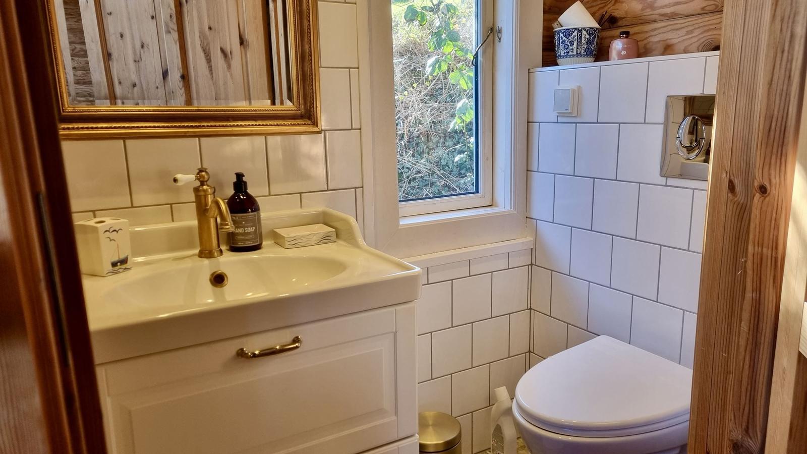 Badezimmer mit Waschbecken, Toilette und Fenster mit Blick auf Vegetation.