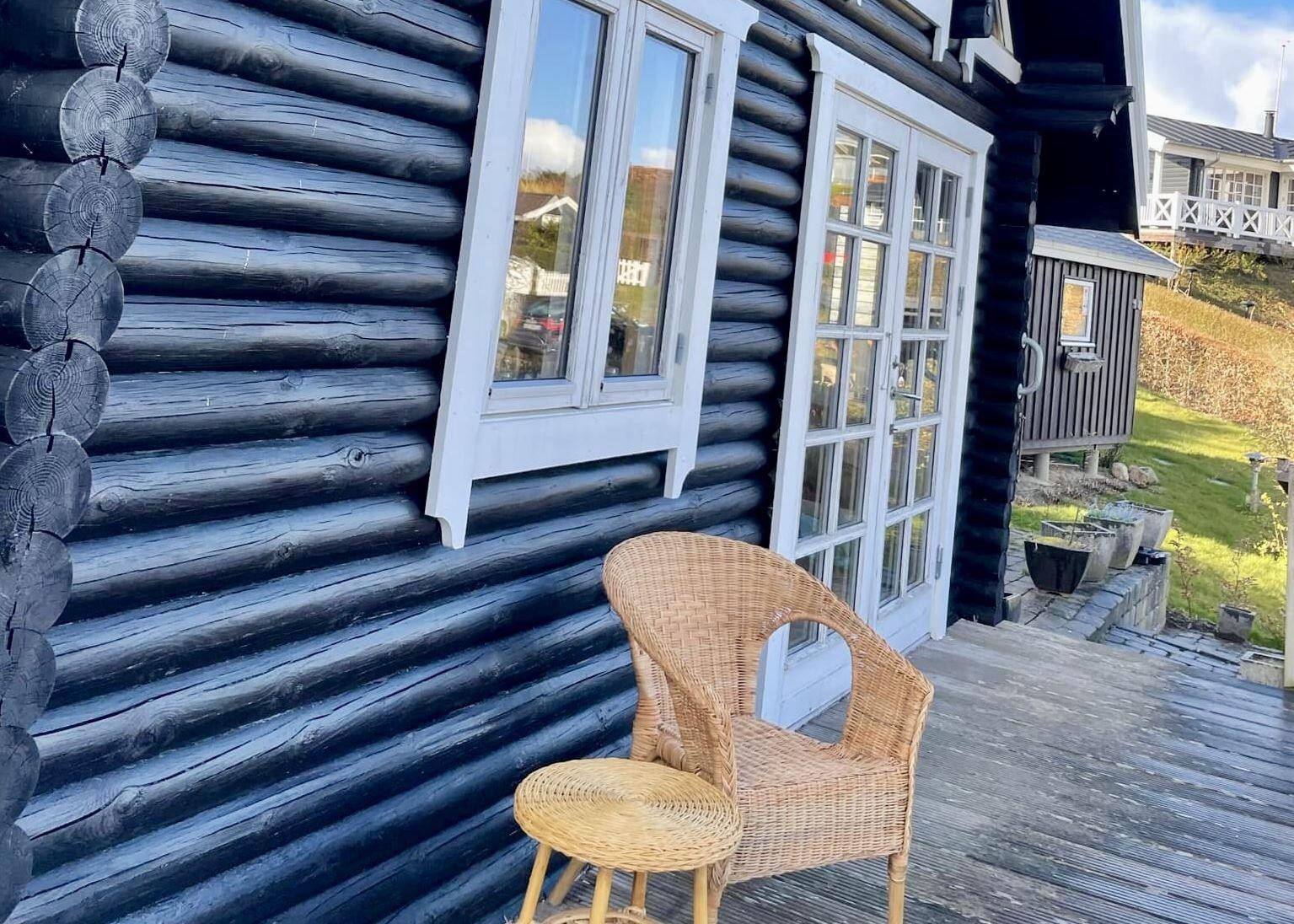 Schwarze Holzhausfassade mit weißen Fenstern und einem Rattanstuhl auf der Terrasse.