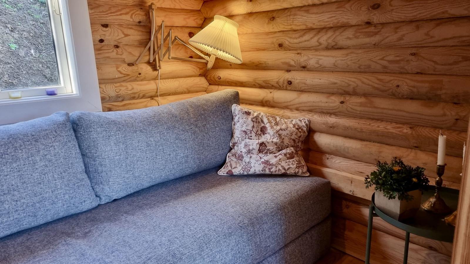 Ein Sofa mit Kissen, Wandlampe und kleiner Tisch mit Pflanze und Kerze.