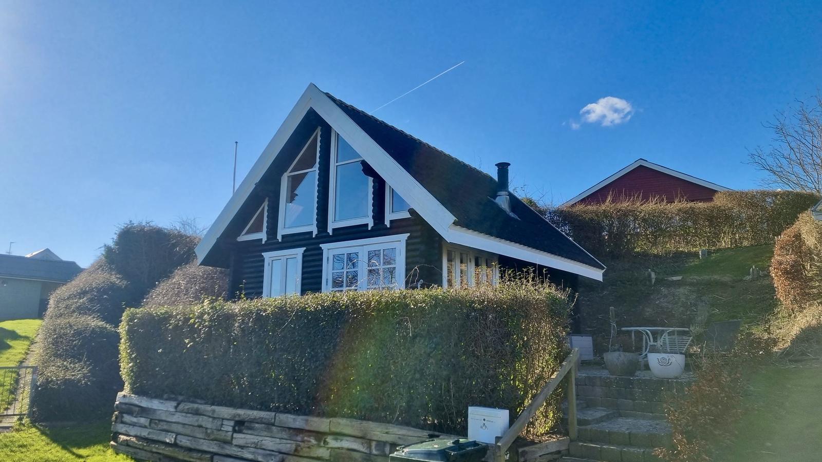 Schwarzes Holzhaus mit weißen Fensterrahmen und Dach, umgeben von Hecken und Grünflächen.