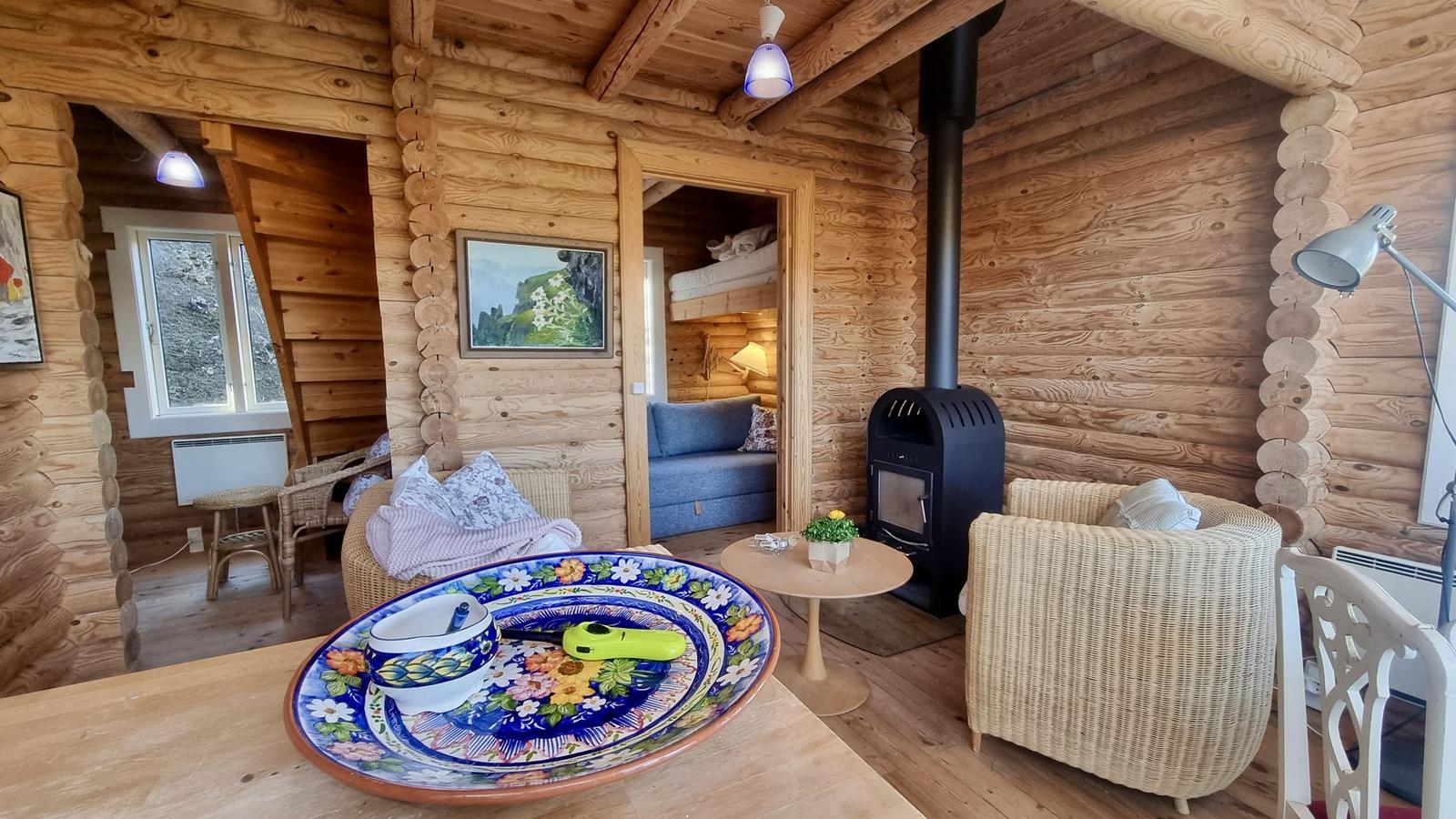 Wohnraum mit Holzwand, Sitzgelegenheiten und Kaminofen. Tisch mit dekorativem Teller.