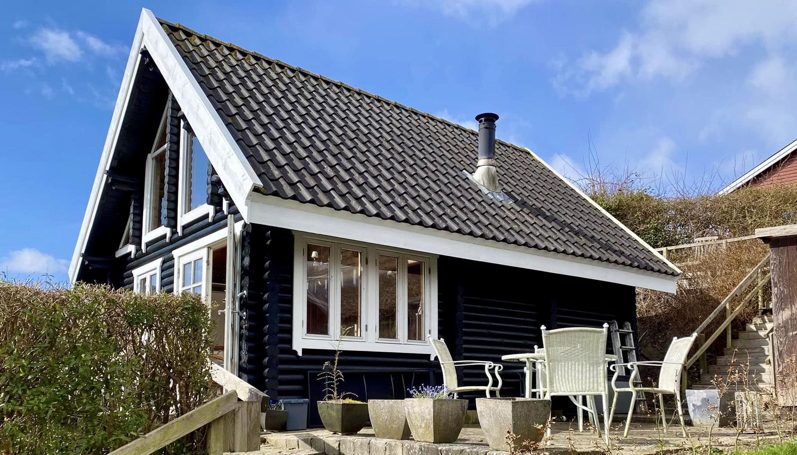 Schwarzes Holzhaus mit weißen Fensterrahmen und Terrasse mit Gartenmöbeln.