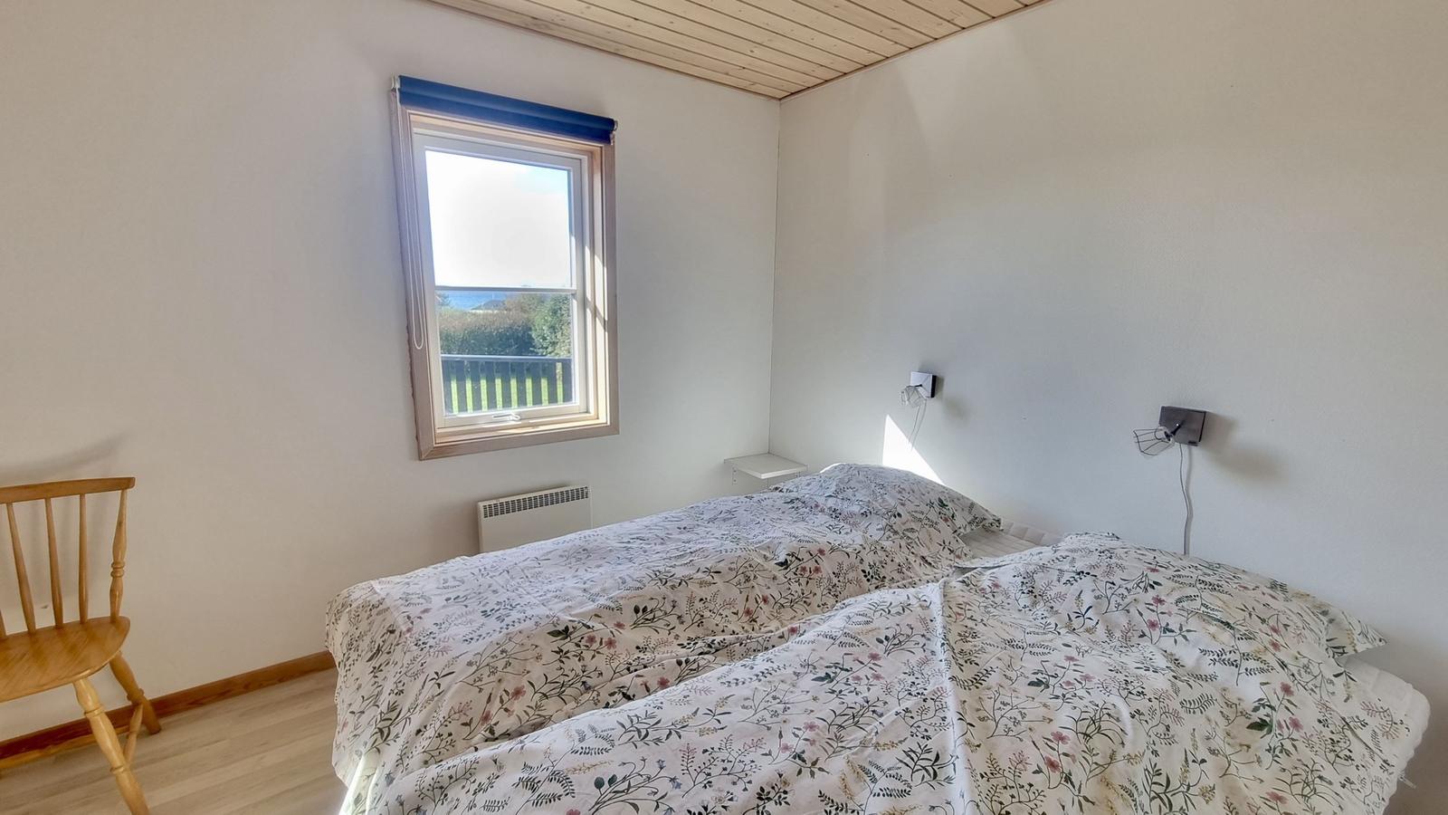 Schlafzimmer mit Doppelbett, Fenster und Holzstuhl.
