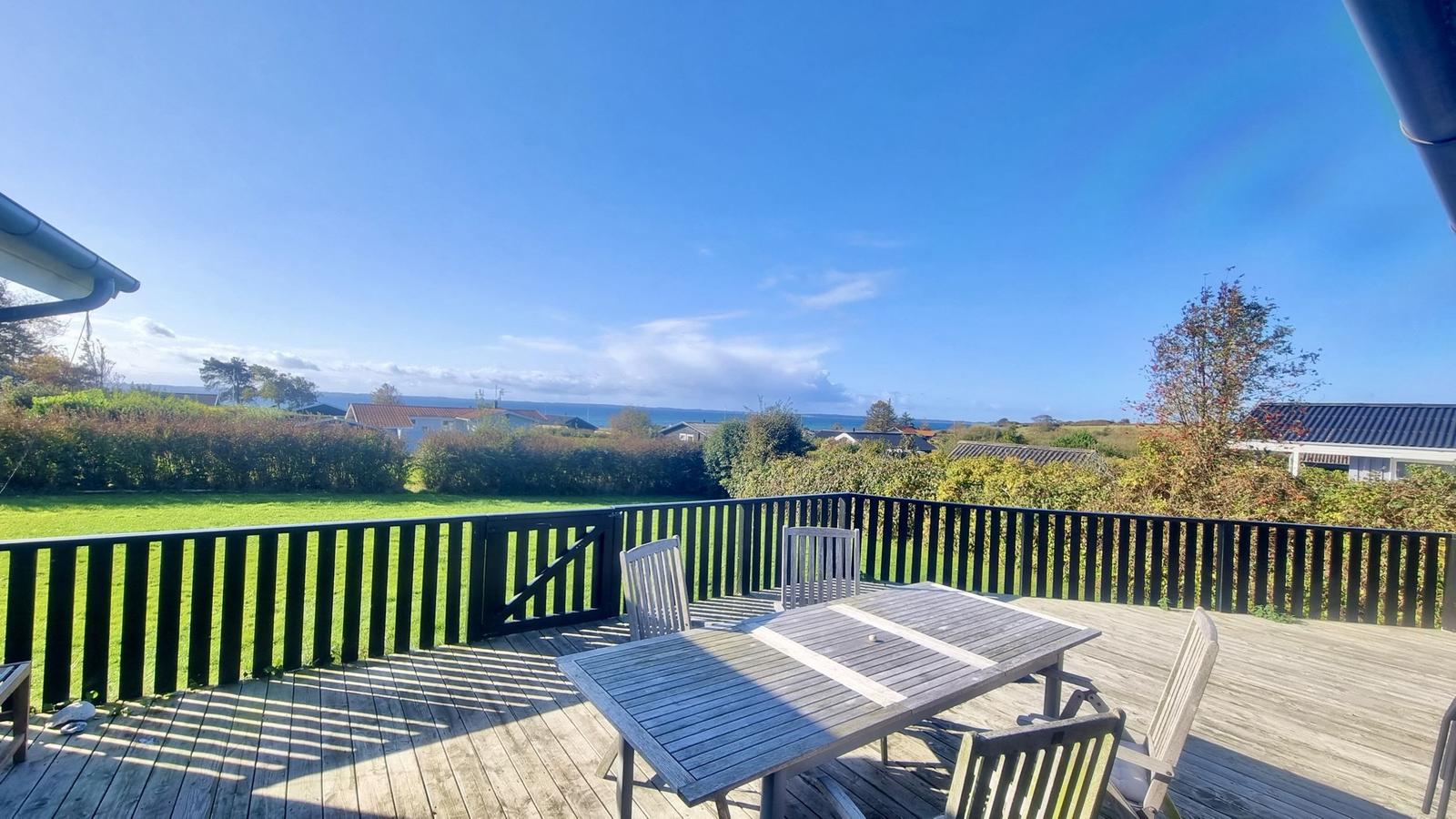 Terrasse mit Tisch und Stühlen, Blick auf Grünfläche und Meer.