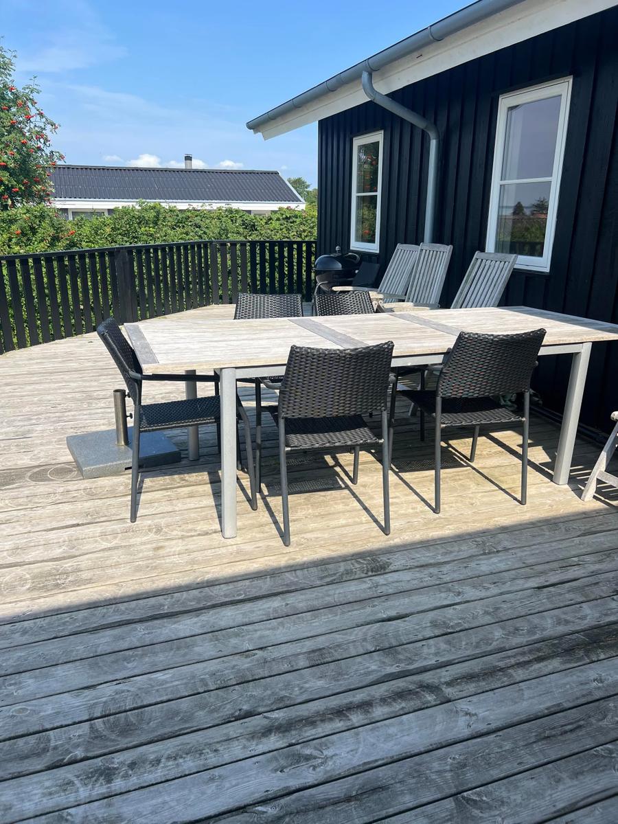 Terrasse mit Tisch, Stühlen und Grill neben schwarzem Haus.