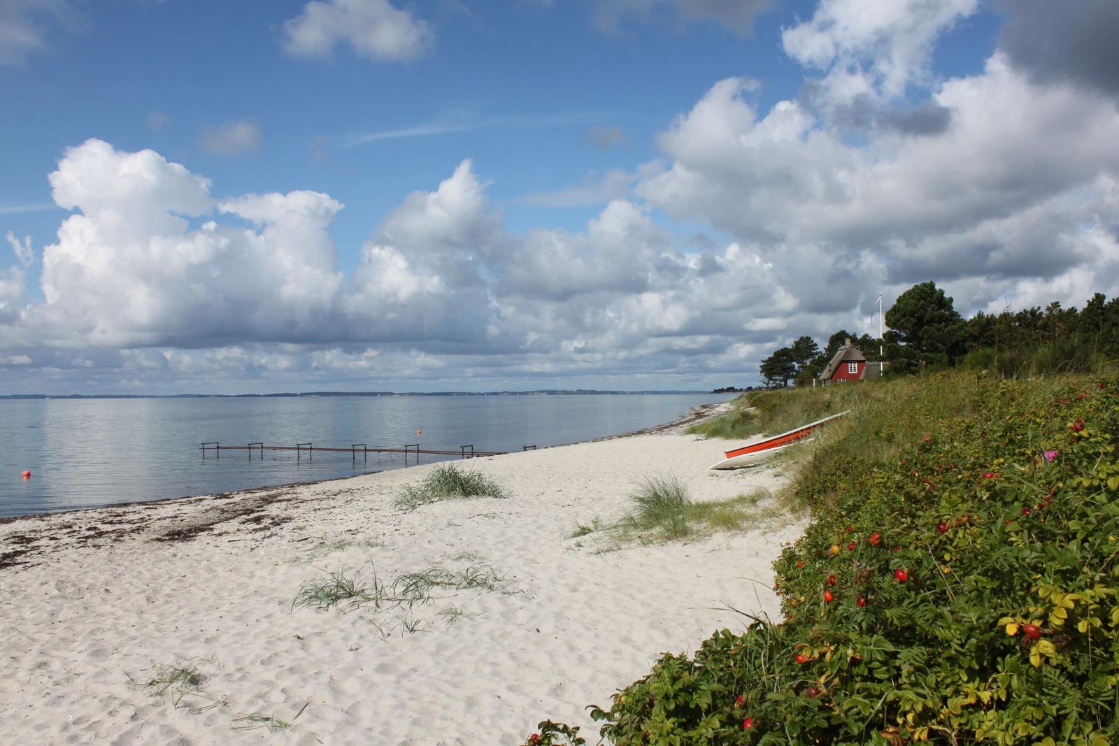 Strand mit weißem Sand, rotem Boot und kleinem Haus am Wasser.