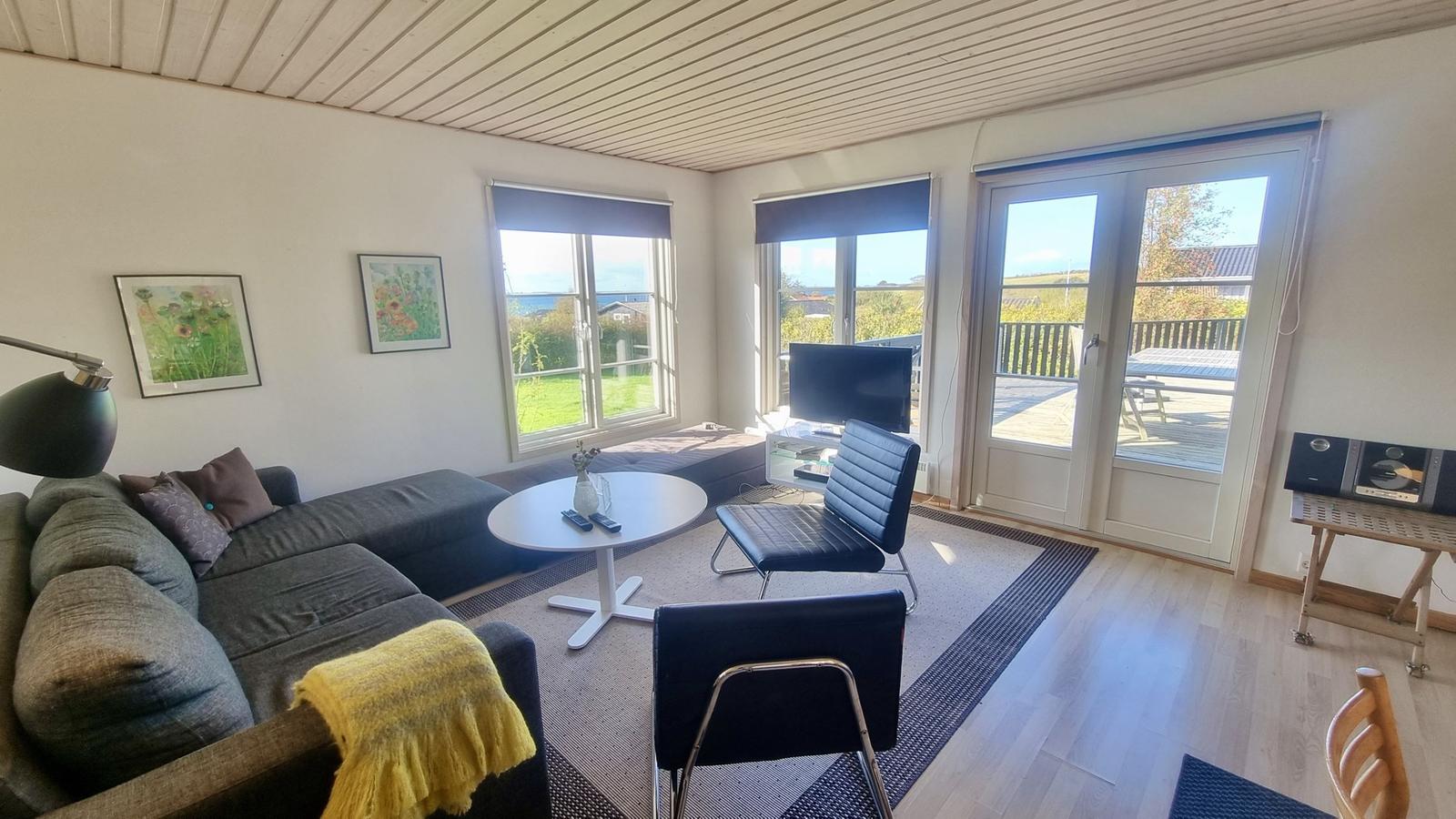 Wohnzimmer mit Sofa, Tisch, Stühlen und Blick auf Balkon und Garten.