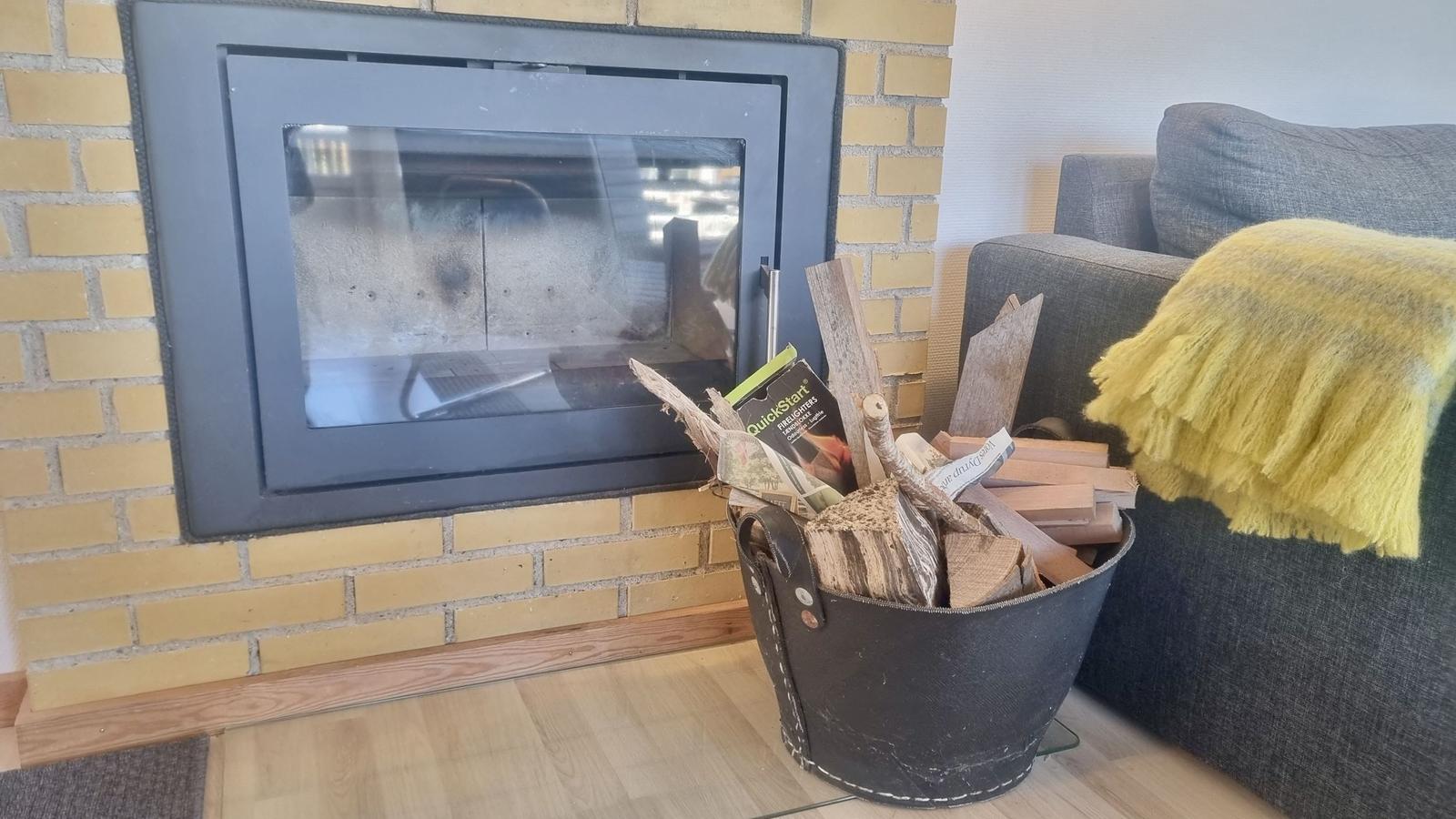 Kamin mit Holz im Eimer neben einem grauen Sofa mit gelber Decke.