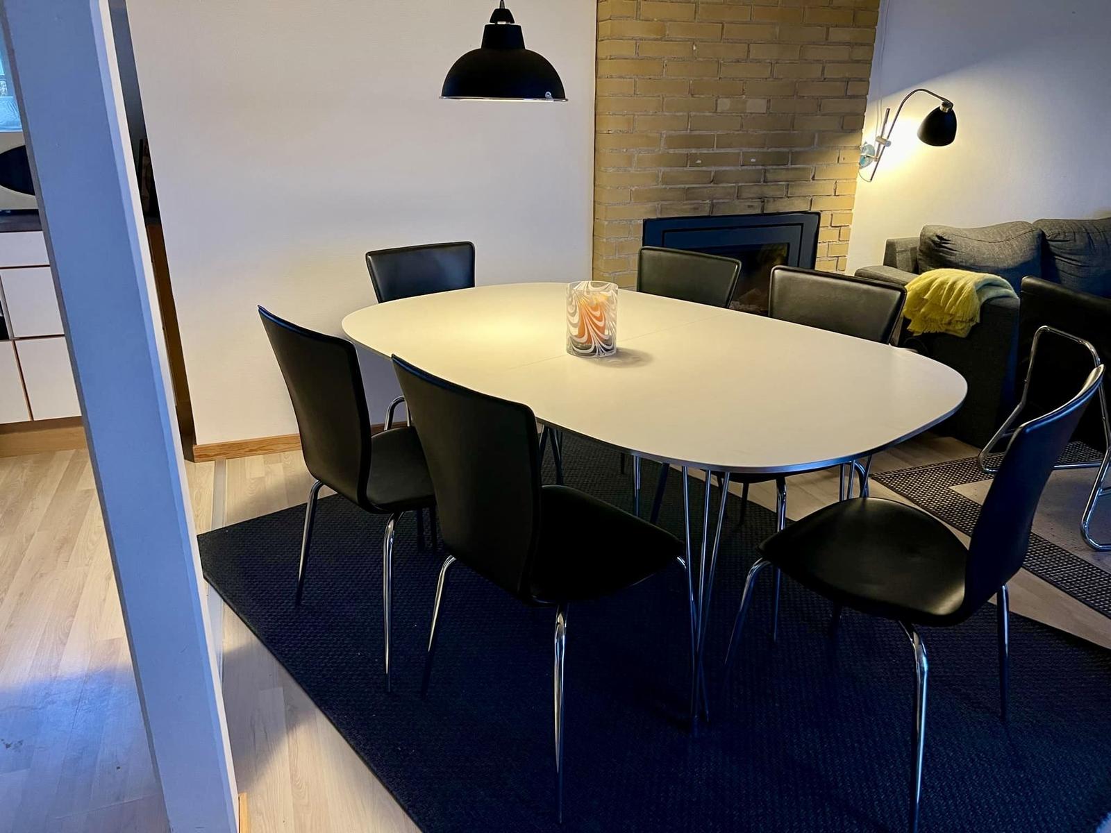 Essbereich mit runden Tisch und schwarzen Stühlen. Hintergrund: Kamin und Sofa.