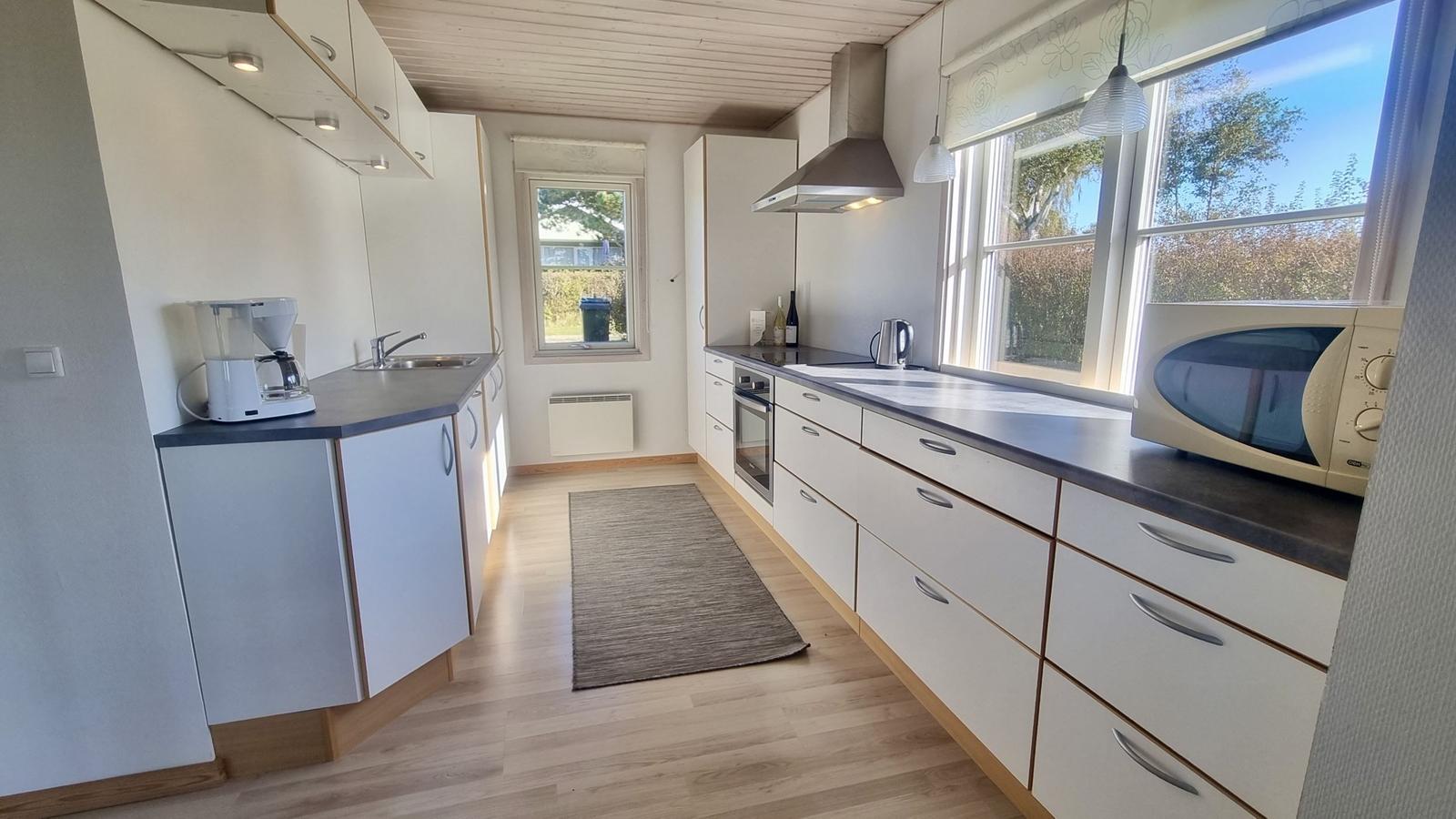 Küche mit weißen Schränken, dunkler Arbeitsplatte und Fenstern mit Blick nach draußen.
