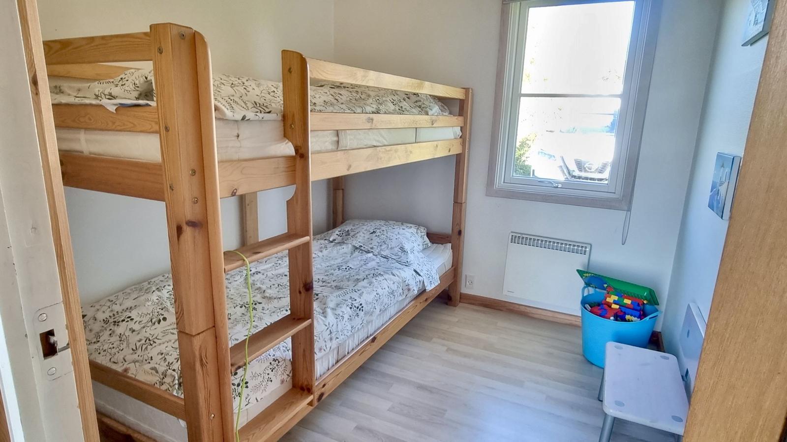 Ein Raum mit einem Holz-Etagenbett, einem Fenster und einem Spielzeugkorb.