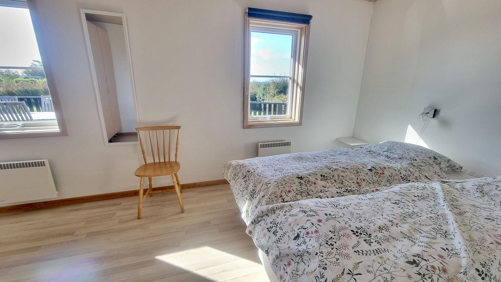 Schlafzimmer mit Doppelbett, Stuhl und Fenstern zur Aussicht.