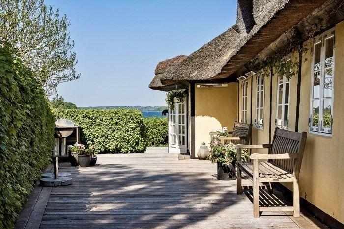 Terrasse mit Holzdielen, Stuhl, Pflanzen und Blick aufs Wasser.