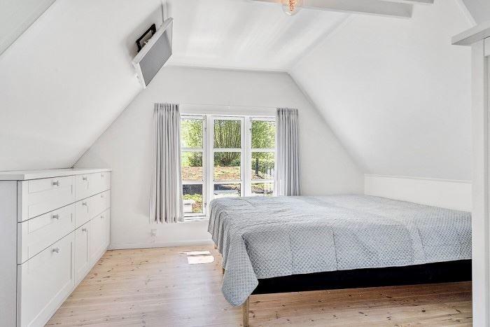 Schlafzimmer mit Dachschräge, großem Bett und Fenster mit Blick nach draußen.