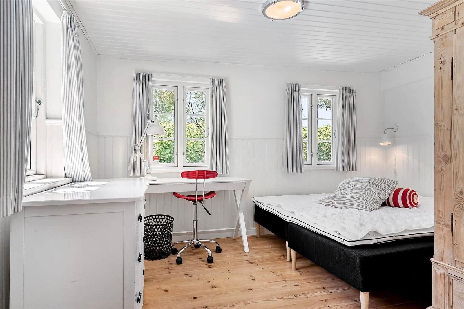 Zimmer mit Bett, Schreibtisch und Fenstern mit Vorhängen.