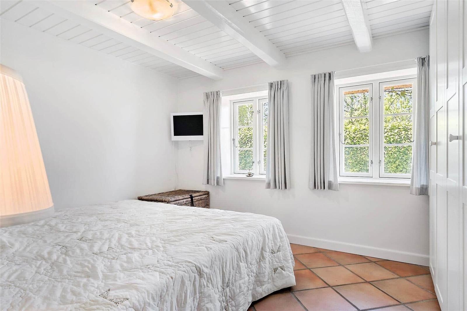 Schlafzimmer mit Bett, Fenstern und Terrakottboden.