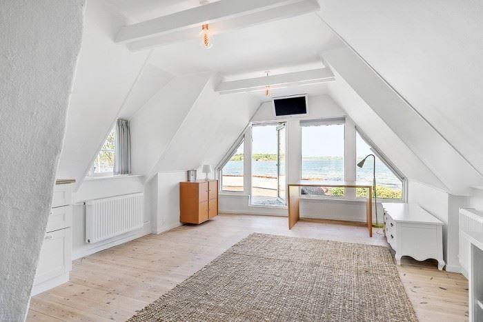 Dachgeschosszimmer mit großem Fenster, Holzboden und weißem Mobiliar.