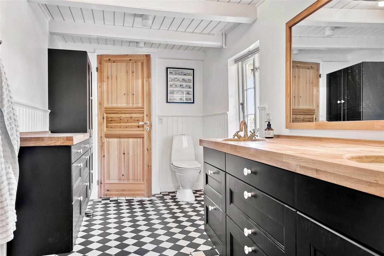 Badezimmer mit Holzwaschtisch, schwarz-weißem Boden und Holztür.