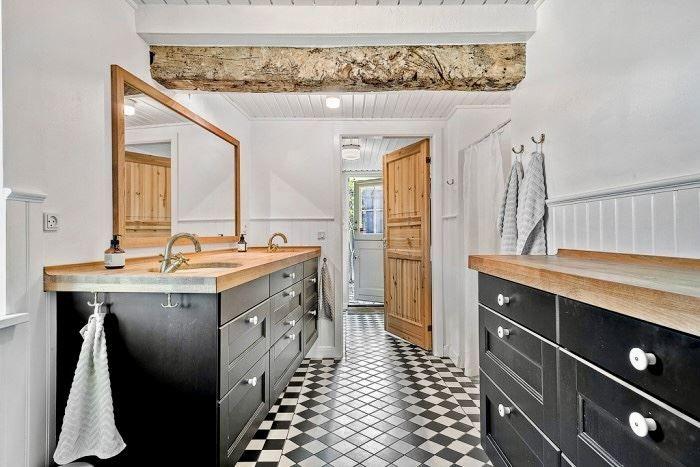 Badezimmer mit zwei Waschbecken, schwarzem Schrank und schwarz-weißem Fliesenboden.