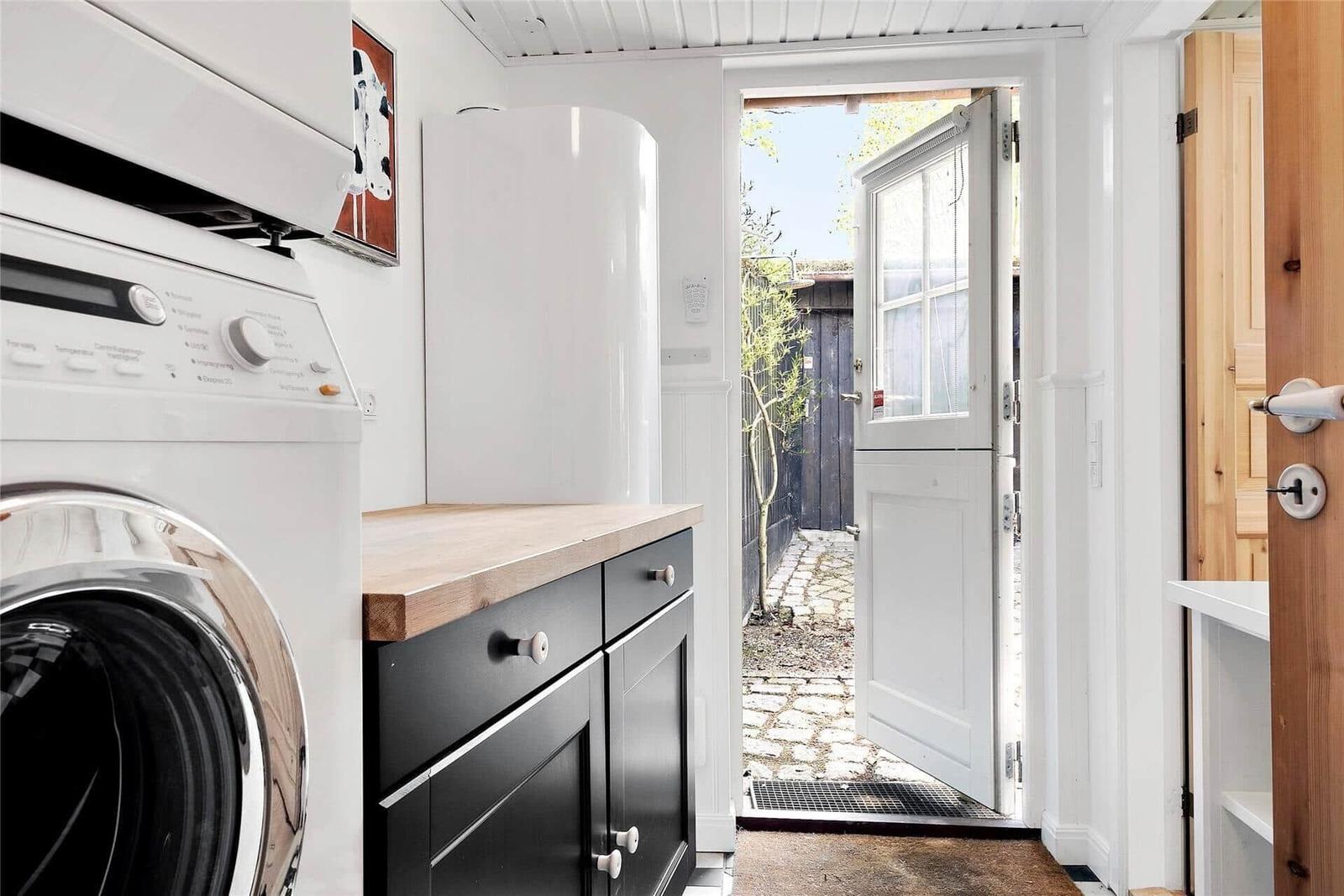 Waschmaschine neben Küchenzeile mit Holzoberfläche und weißer Tür zum Garten.