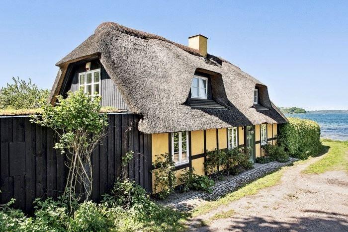 Dorfhaus mit Strohdach, gelben Wänden und Fenstern am Wasser