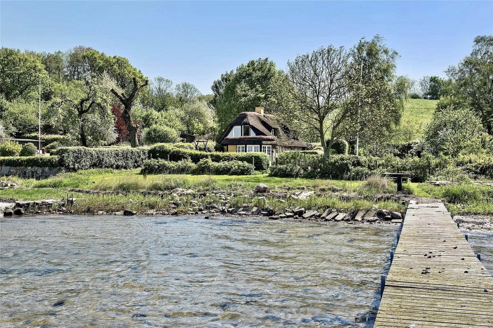 Haus mit Strohdach am Wasser mit Steg und Grünflächen.