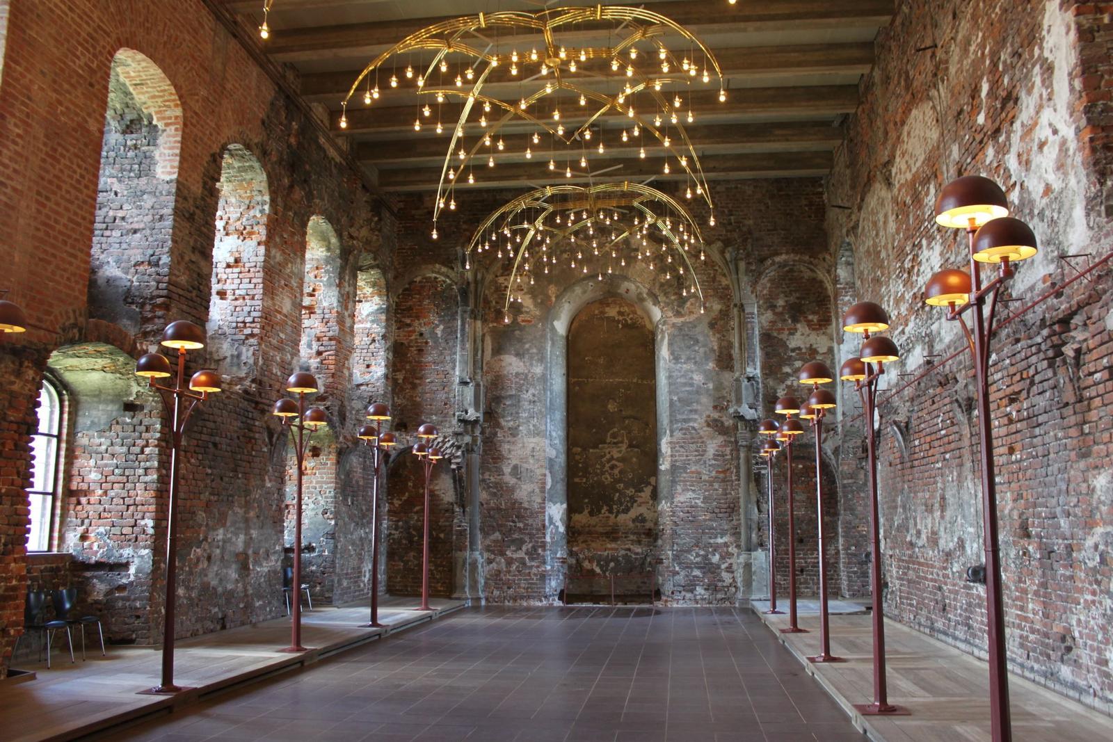 Großer Raum mit Backsteinwänden, modernen Lampen und goldenen Deckenleuchten.