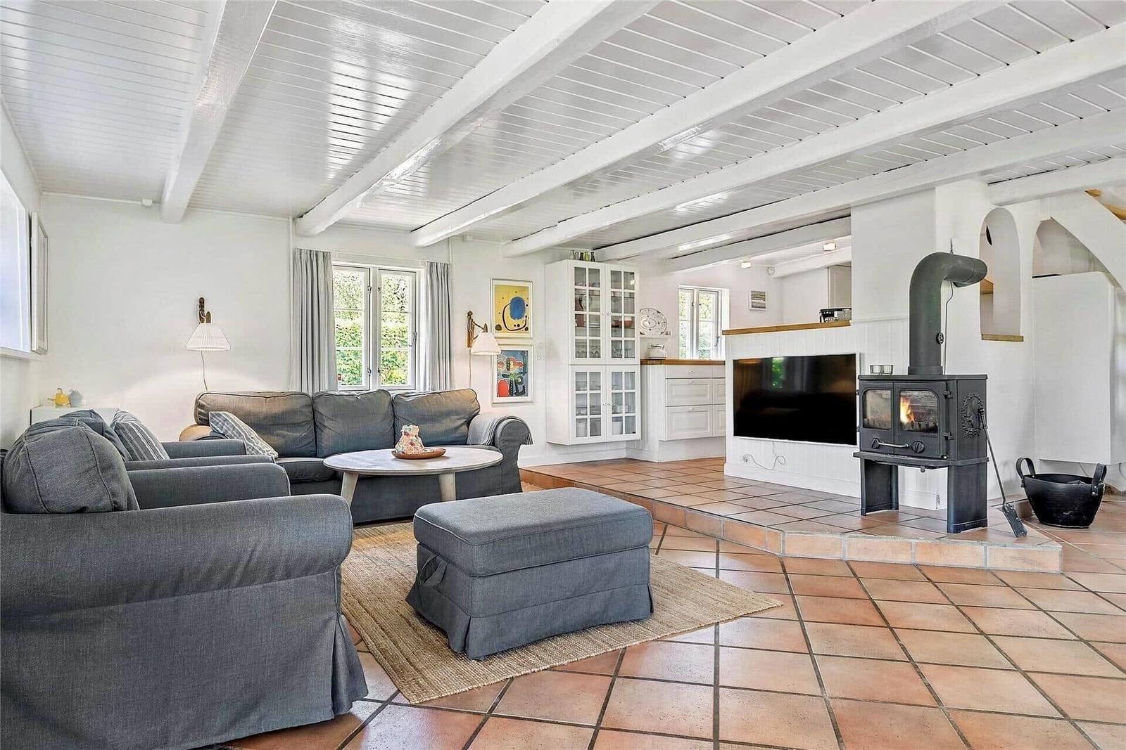 Wohnzimmer mit Sofa, Sitzbank und Kaminofen. Holzboden und weiße Deckenbalken.