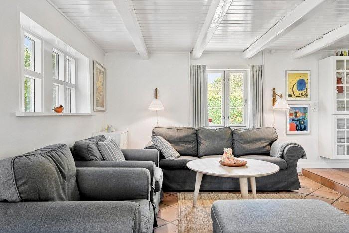 Wohnzimmer mit grauem Sofa, runden Tisch und Fenstern.