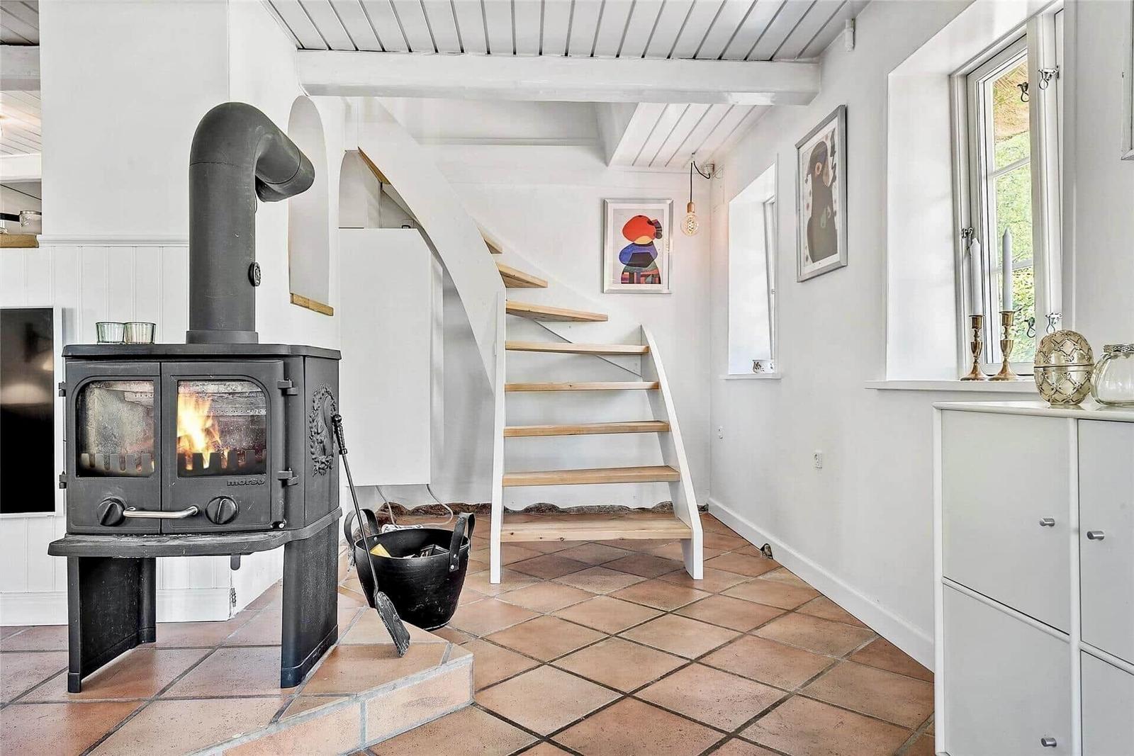 Raum mit Kaminofen, Treppe und Fenster. Boden aus Terrakottafliesen.