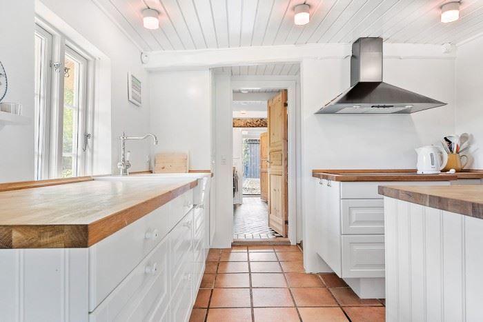 Küche mit Holzplatten, weißen Schränken und Terrakottboden