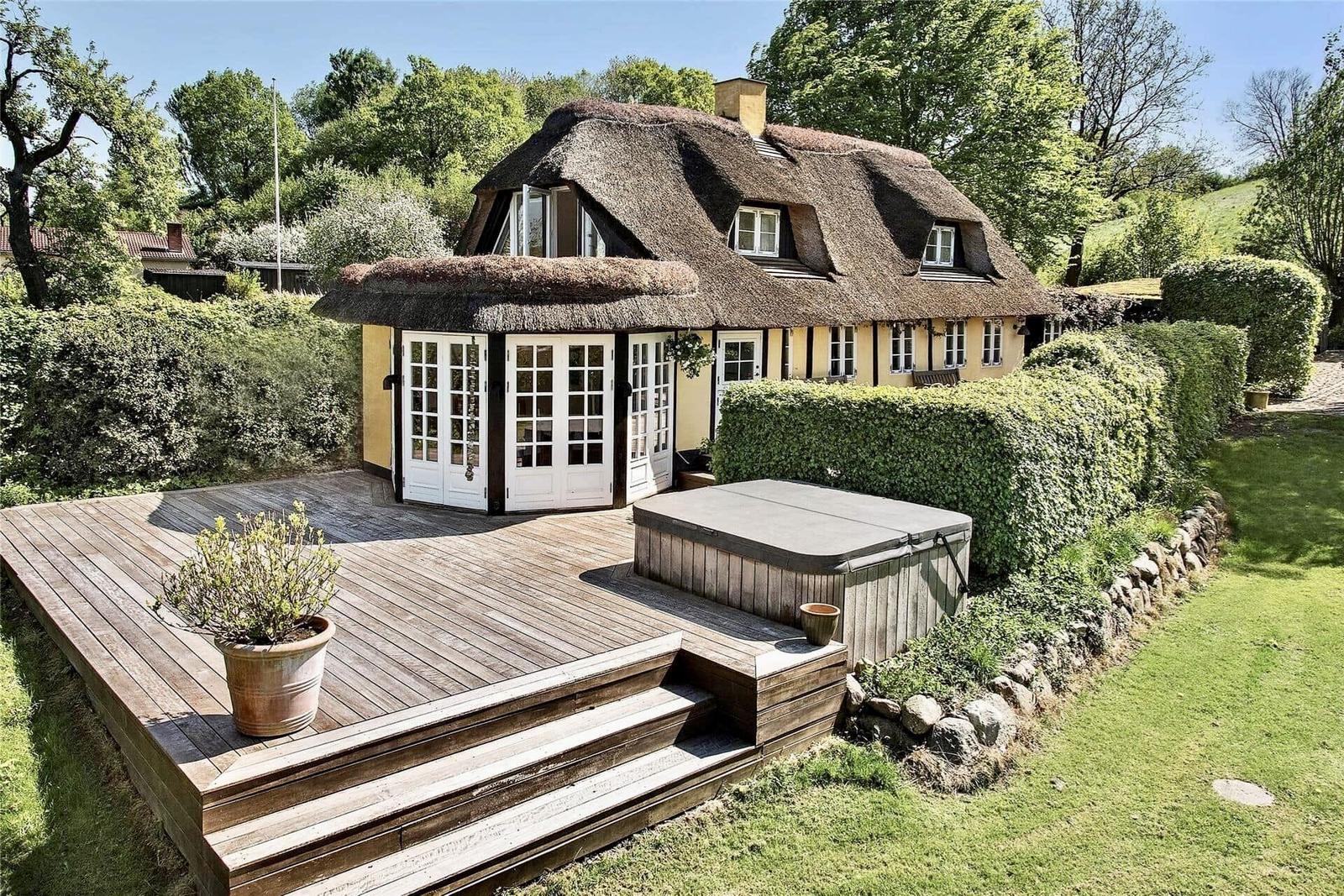 Haus mit Strohdach, Holzterrasse und Whirlpool im Garten.