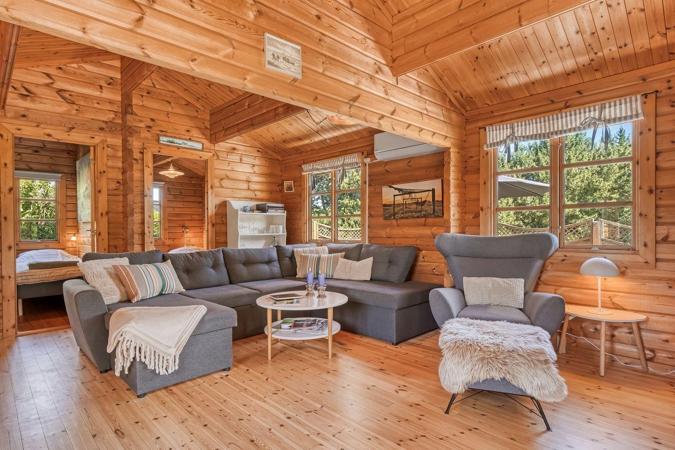Wohnzimmer mit Holzdecke, Sofa und Sessel. Durch Fenster Blick auf Garten.