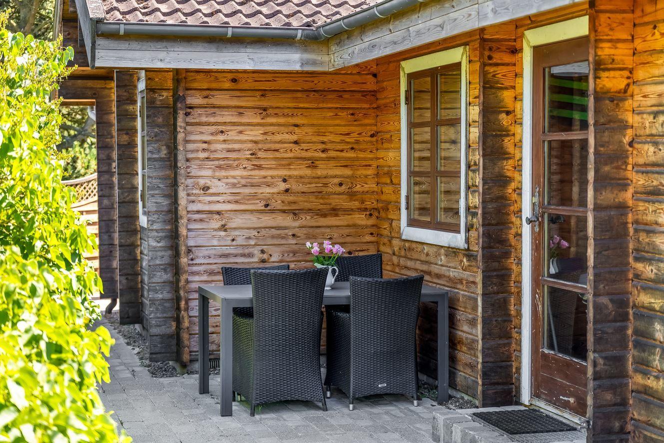 Terrasse mit Tisch und Stühlen neben Holzhaus mit Fenster und Tür.