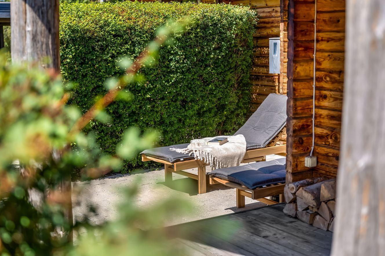 Terrasse mit Liegestühlen und Holzwand. Hintergrund: grüner Heckenbereich.